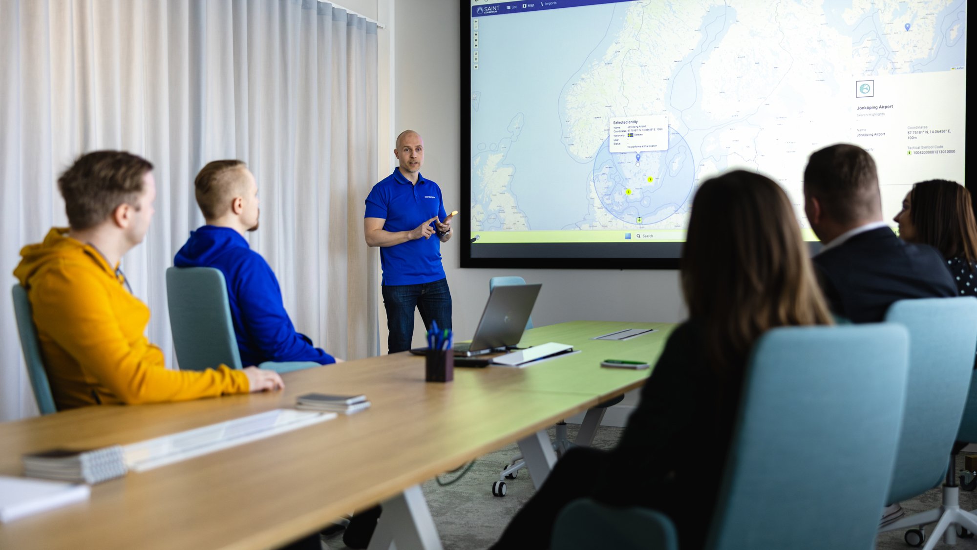 Demonstration of SAINT SIGINT Database solution with people around the rable.