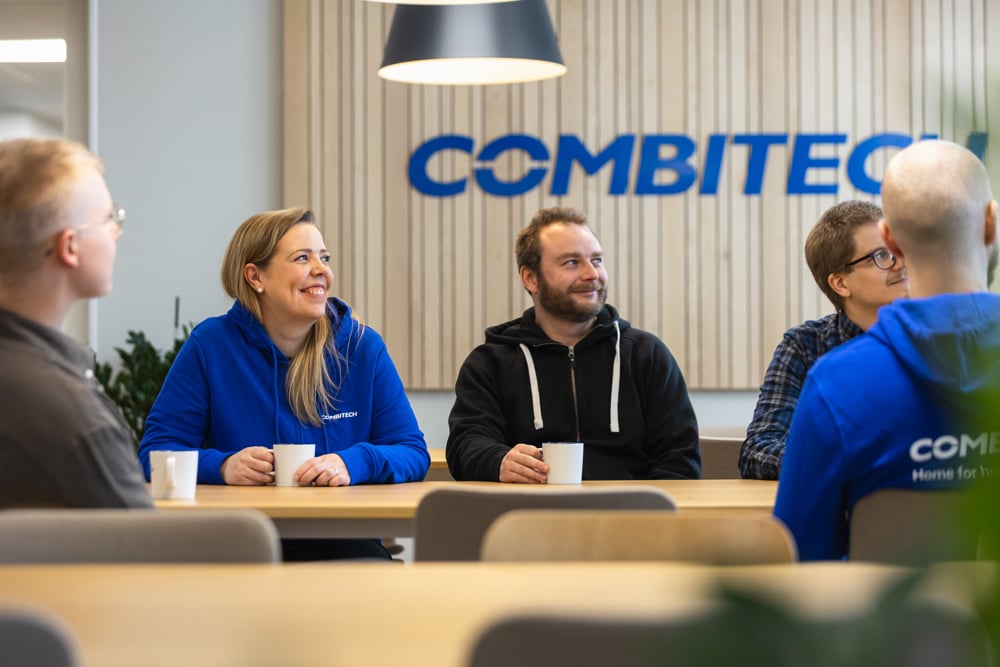 Combitech employees smiling and and having a conversation around the table.